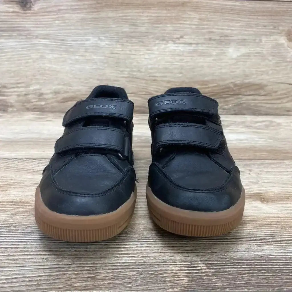 Front view of Geox Arzachboy toddler sneakers showing black leather upper, double hook and loop straps and gum rubber soles on wood floor