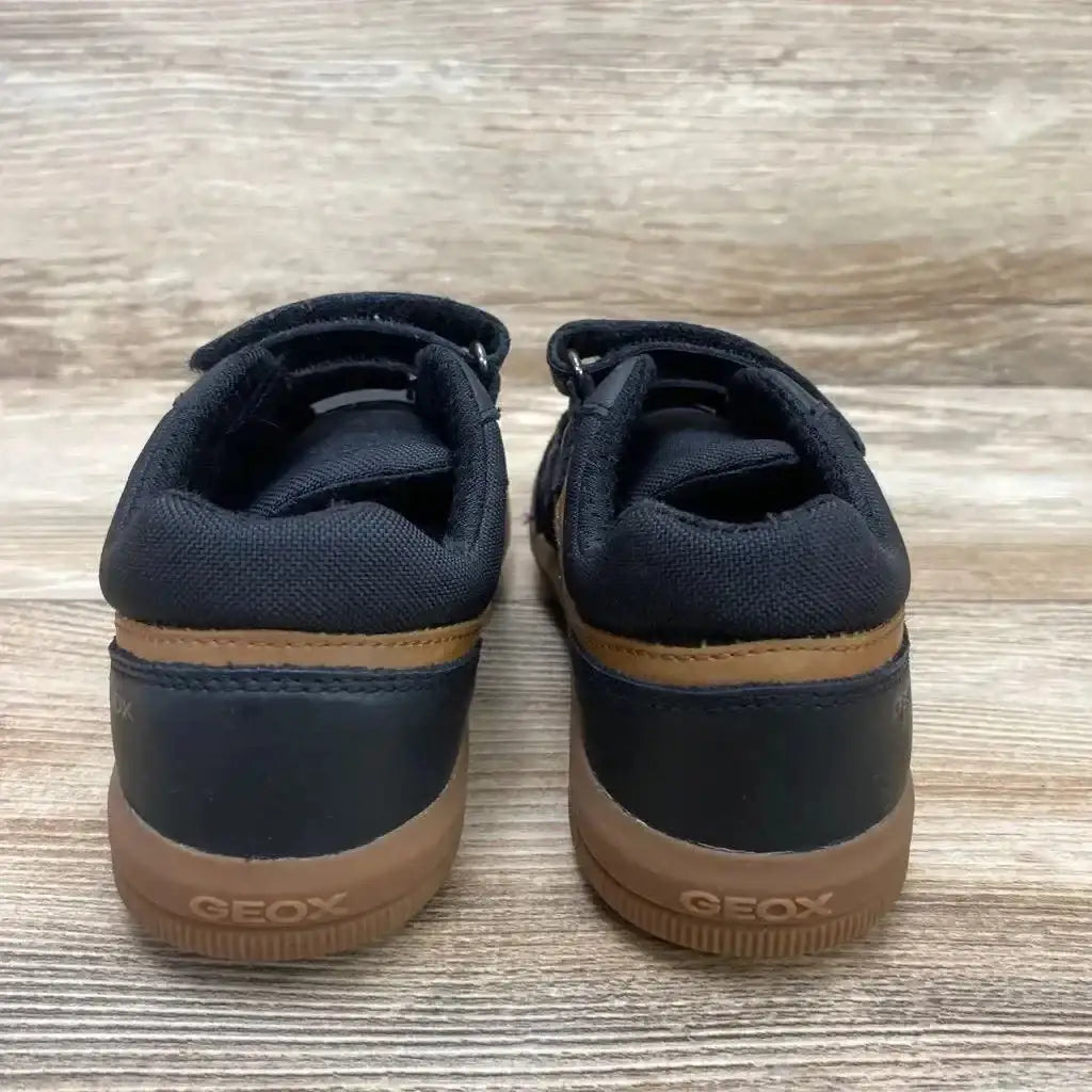 Rear view of black Geox Arzachboy toddler sneakers showing brown trim, rubber soles with GEOX logo on wood surface