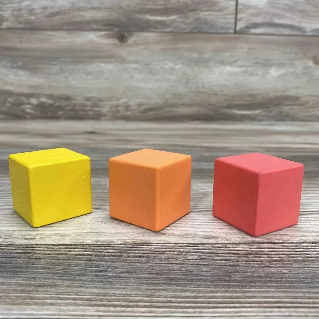 Front view of Lovevery 3-piece first blocks showing yellow, orange, and red wooden cubes on a wood tabletop