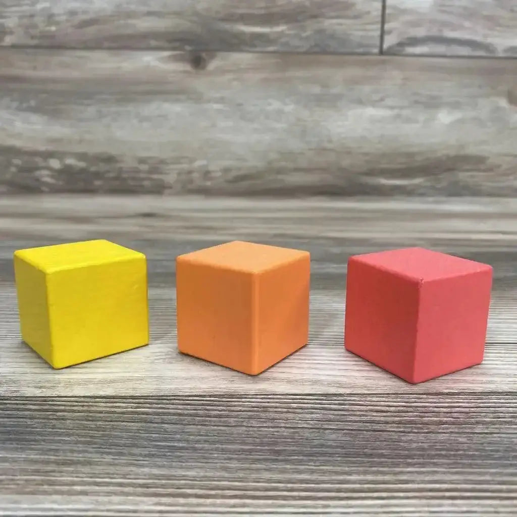Front view of Lovevery 3-piece first blocks showing yellow, orange, and red wooden cubes on a wood tabletop