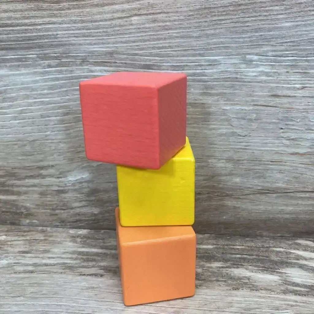 Stacked view of Lovevery 3pc First Blocks showcasing red yellow and orange painted wooden cubes on wood plank floor