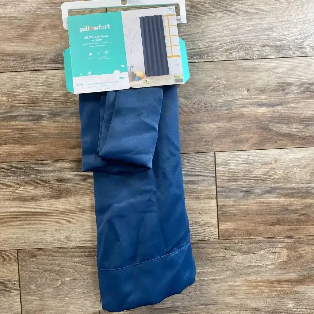 Top-down view of navy Pillowfort blackout curtain folded with packaging label visible and stitched hem on wood floor background