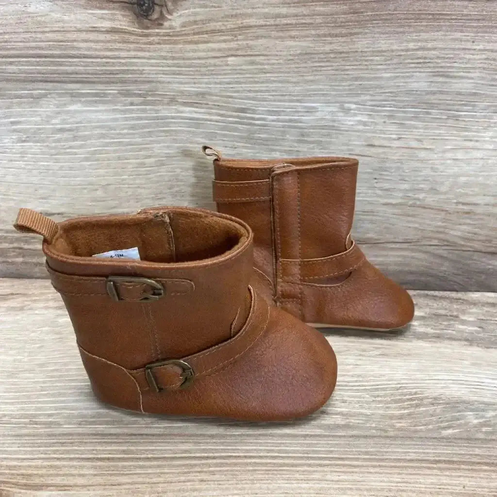 Three-quarter view of brown faux-leather toddler tall booties (size 3/4C) showing side buckles and pull tabs on light wood background