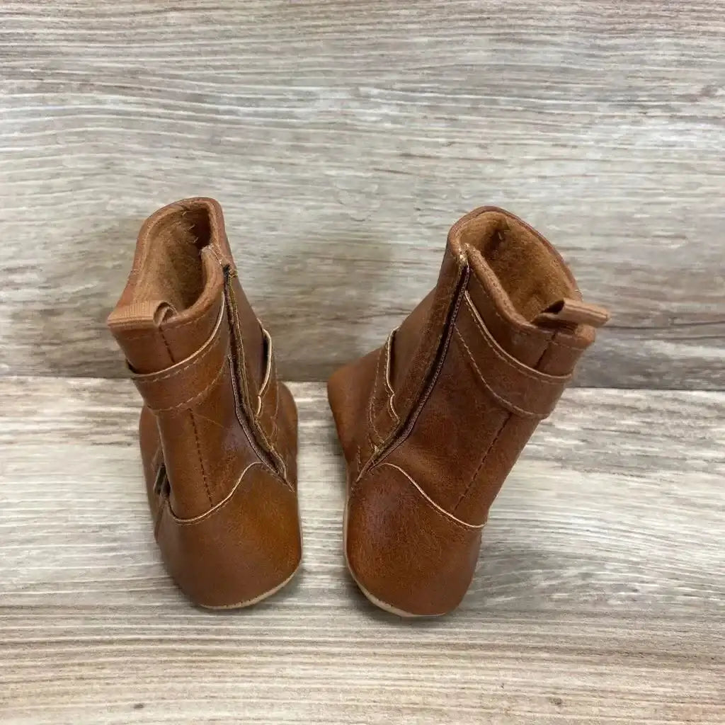 Rear view of brown faux-leather baby bootie pair with back pull tabs, side zippers and buckled straps on wood background