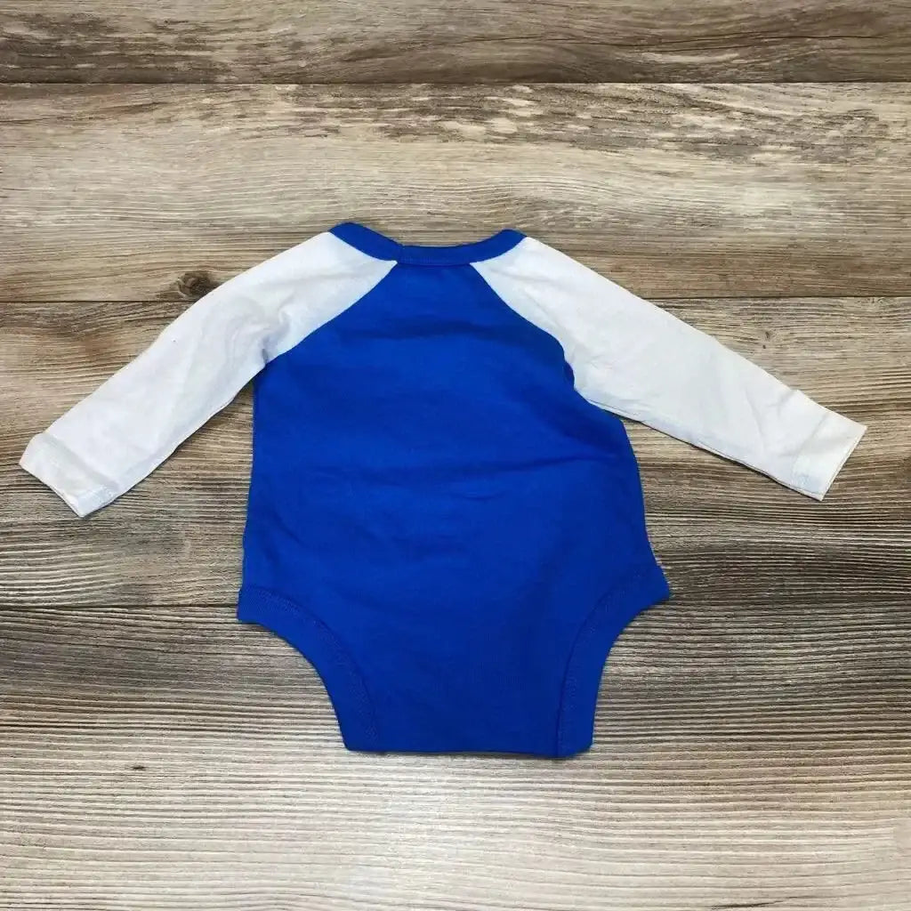 Top-down view of newborn blue bodysuit with white raglan long sleeves on wood background