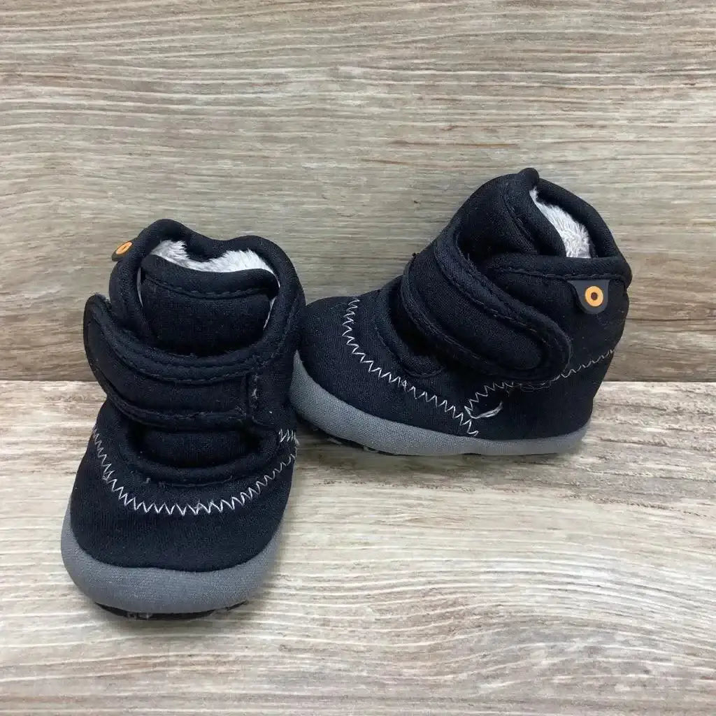 Three quarter view of Bogs Elliot II boots in black with hook and loop straps fleece lining and grey sole on wood plank floor