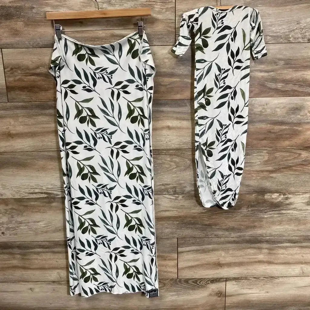 Top-down view of Milkmaid Goods swaddle and knotted gown set in Oliver, showing a black and green leafy print on wood