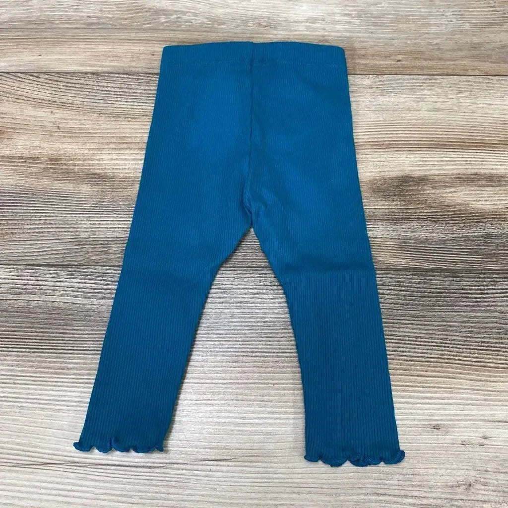 Flat lay of teal ribbed baby leggings (6m) showing lettuce-edge hems and elastic waistband on light wood background