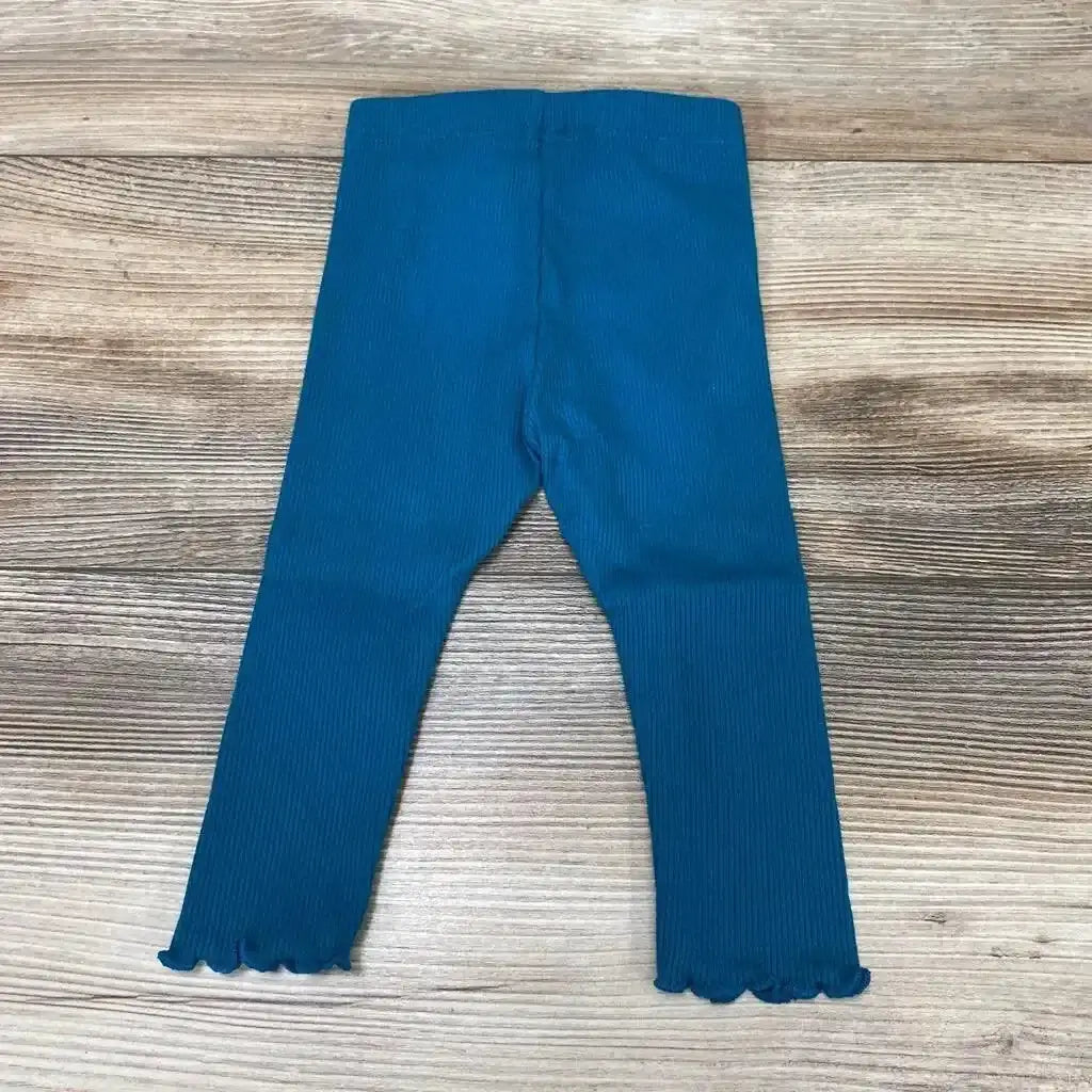 Flat lay of teal ribbed baby leggings (6m) showing lettuce-edge hems and elastic waistband on light wood background