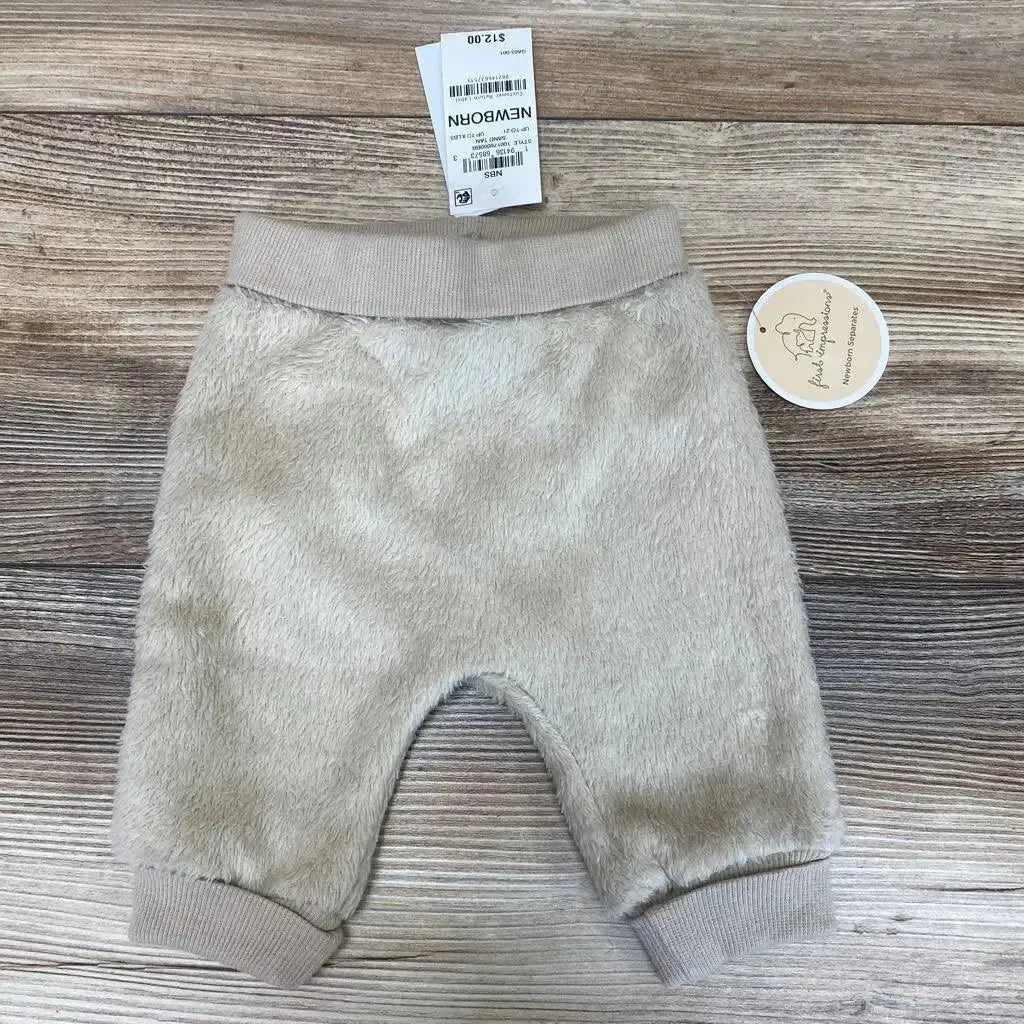 Front view of First Impressions faux sherpa pants in beige newborn size showcasing ribbed waist and cuffs with hangtags on wood plank floor