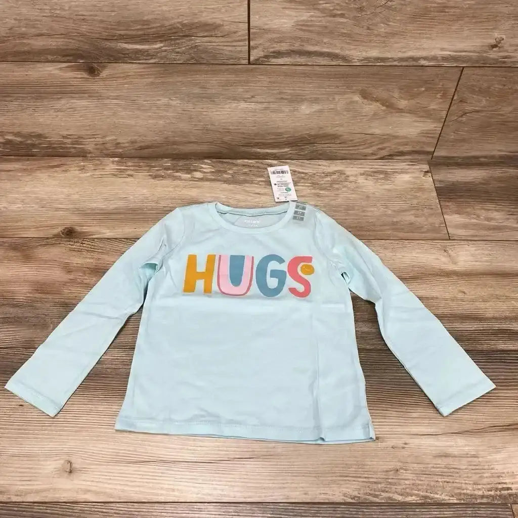Flat lay of NEW Carters Hugs long sleeve shirt size 3T in light blue with multicolor HUGS print and hangtag on wood plank floor
