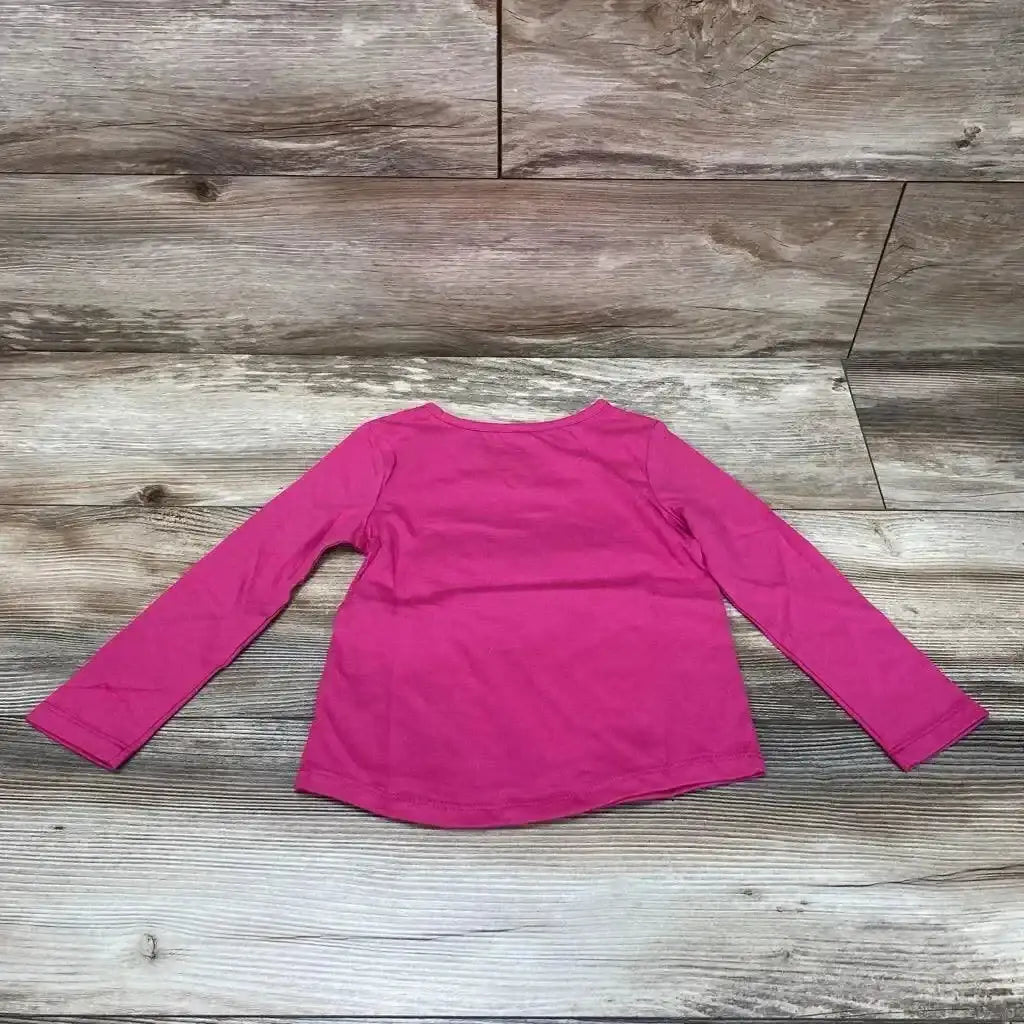Back view of Grandma's Cookie 3T long-sleeve toddler shirt showing solid pink fabric and rounded hem on wood background