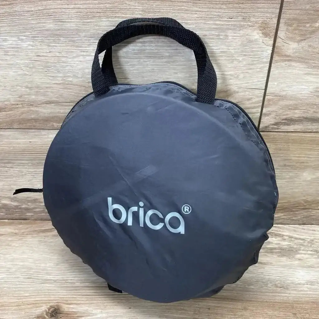 Front view of grey Brica infant car seat comfort canopy packed in round carry bag showing Brica logo and handles on wood floor background