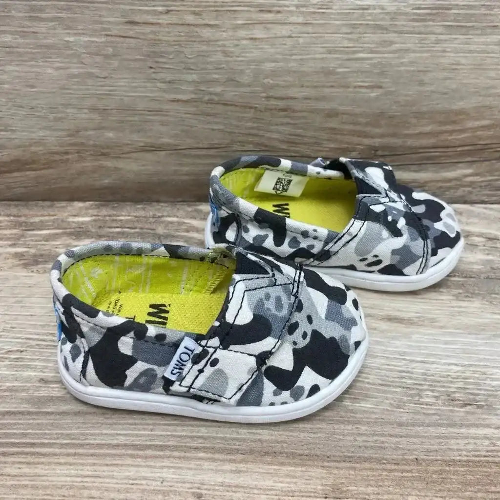 Side view of Toms Wildaid panda camo slip-on shoes in black white and gray with yellow insole on wood plank floor