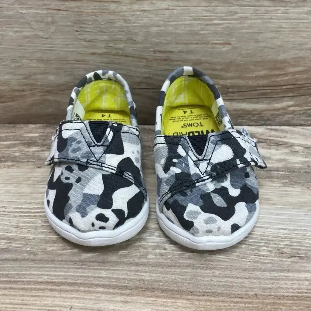 Front view of toddler Toms slip-on shoes showcasing grey and white camo panda print and Velcro strap with wood background