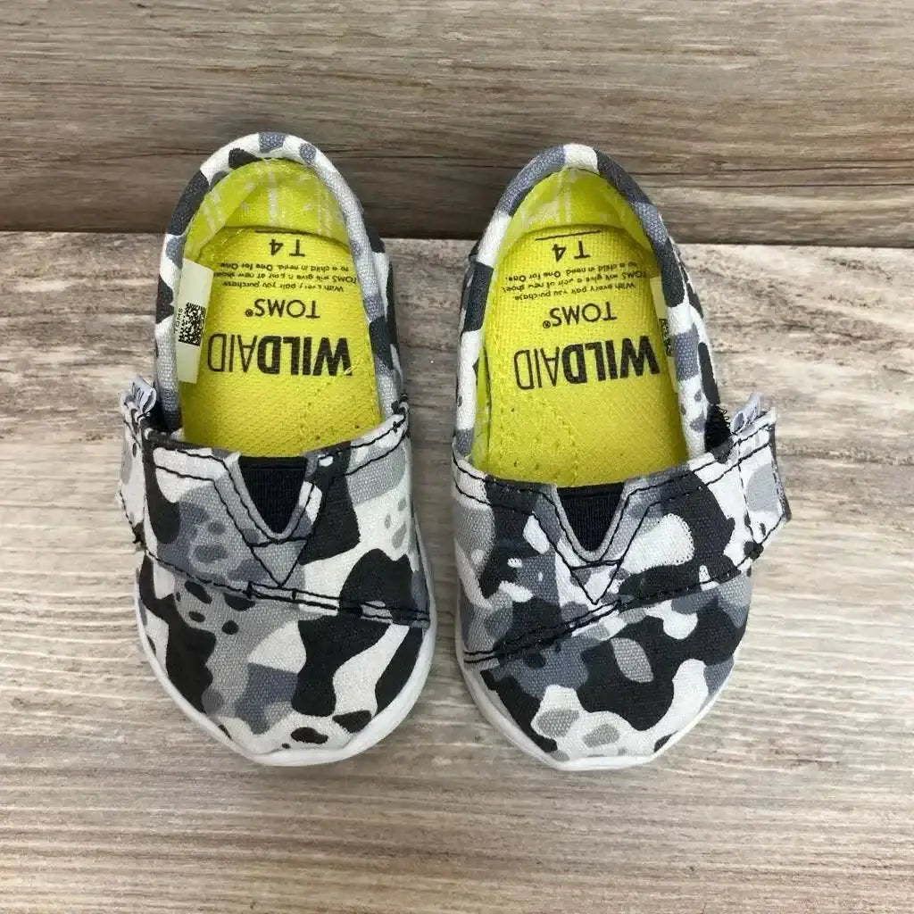 Top view of Toms Wildaid Camo Panda shoes showcasing black white and grey camo canvas slip-ons with yellow Wildaid insoles on wood plank floor