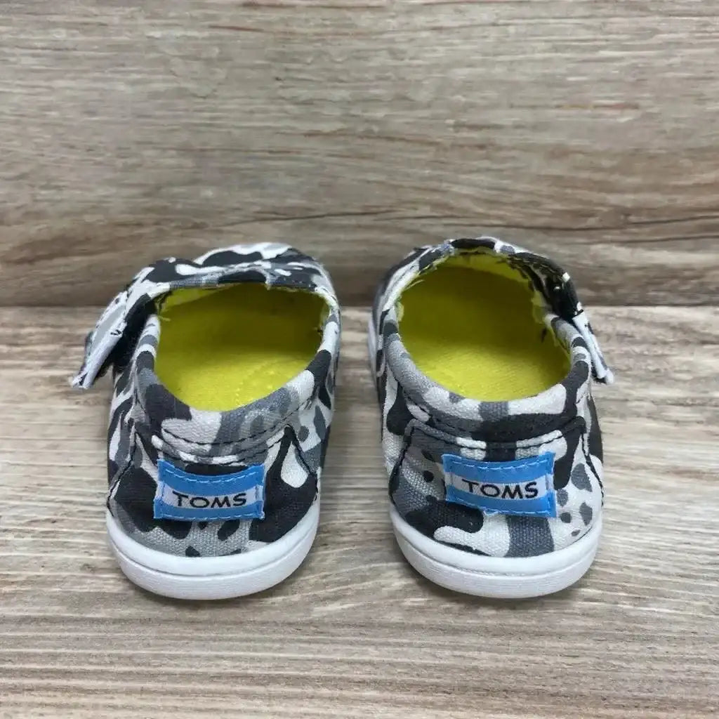 Back view of Toms Wildaid Camo Panda Shoes in black and white panda print with yellow lining and blue TOMS heel label on wood plank floor