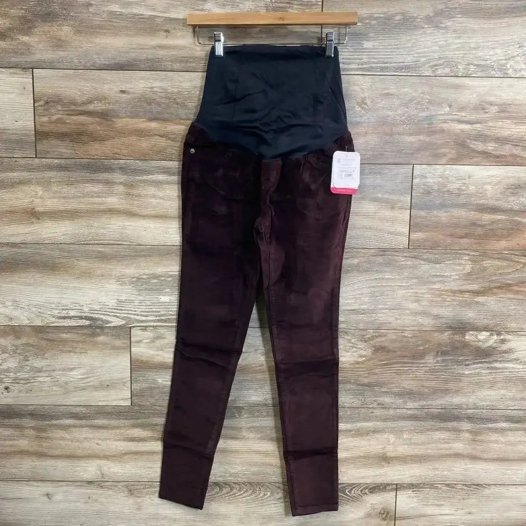 Front of Isabel burgundy maternity crossover-panel skinny jeans with black belly panel on hanger against wood floor