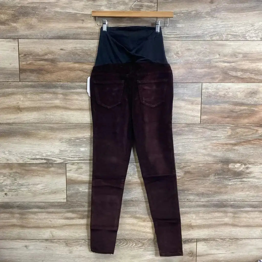Back view of burgundy Isabel maternity skinny jeans with black crossover belly panel and rear pockets on wood background