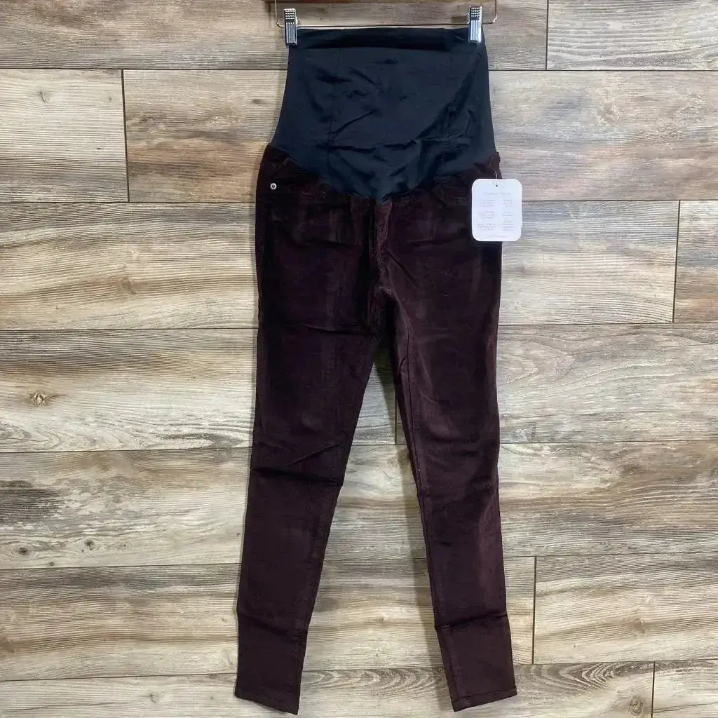 Front view of burgundy Isabel maternity skinny jeans size 00 showing crossover belly panel, hanging on wood plank background