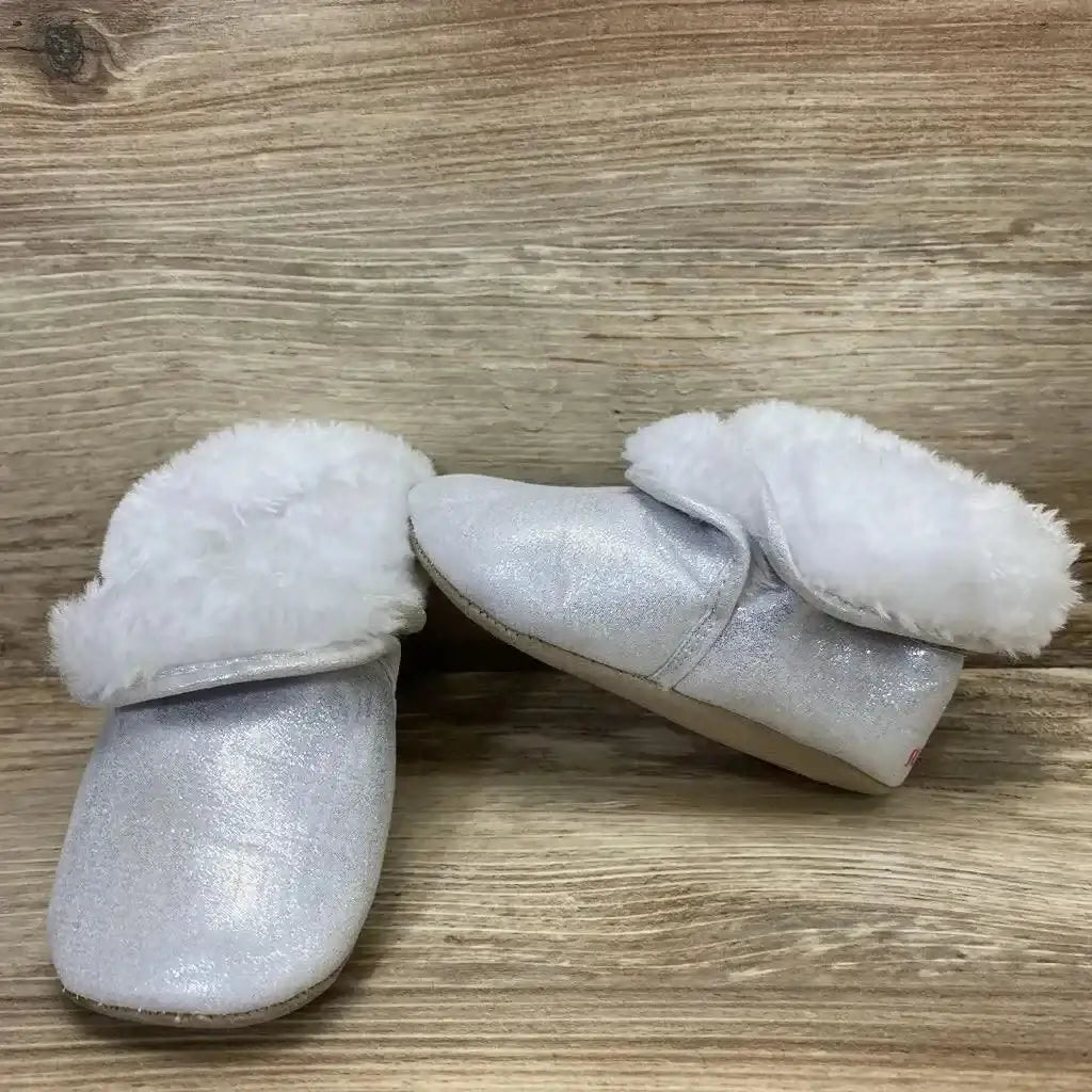 Three-quarter view of Surprize shimmer ankle booties in silver with white faux fur cuff on wood plank floor