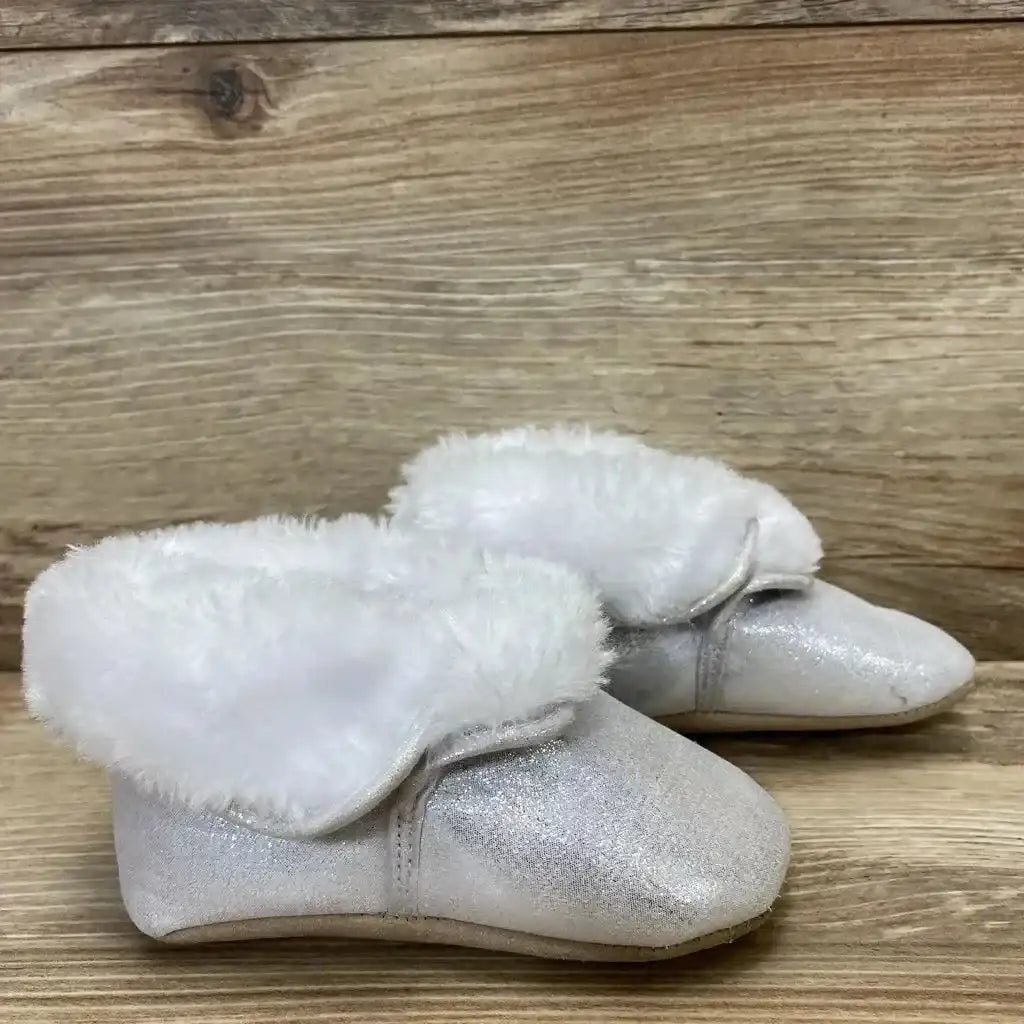 Angled view of silver baby ankle booties size 4C with glitter shimmer and white faux fur cuff on wood background