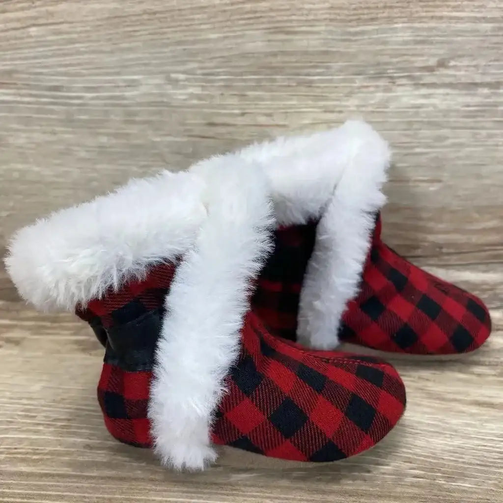 Side view of Robeez Jack soft sole baby booties in red and black plaid with white faux fur cuff on wood background