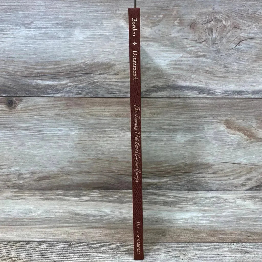 Spine view of The Journey That Saved Curious George hardcover, brown cloth spine with gold title on wood background