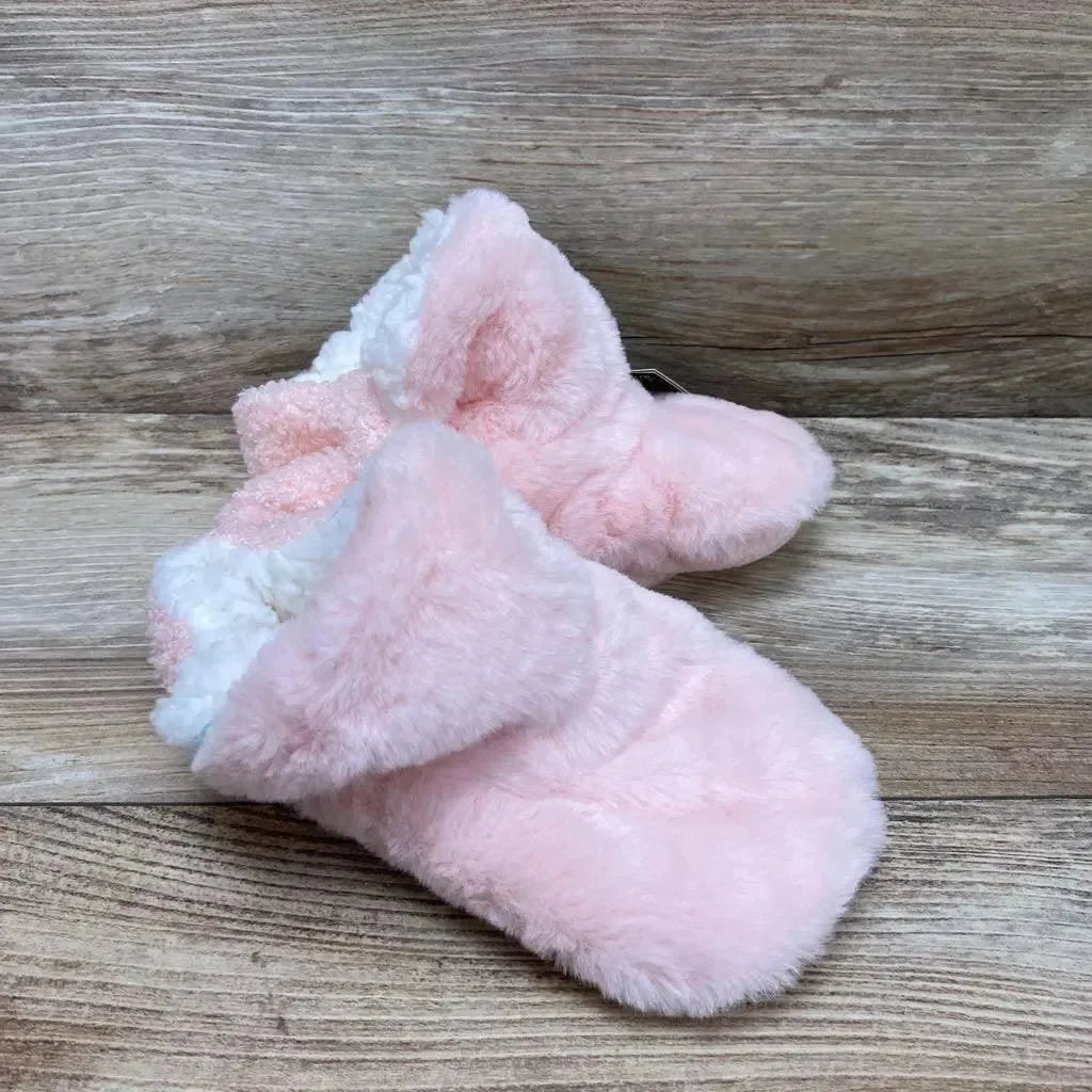 Three-quarter view of pink infant plush slippers showcasing white sherpa lining and gripper soles on light wood background