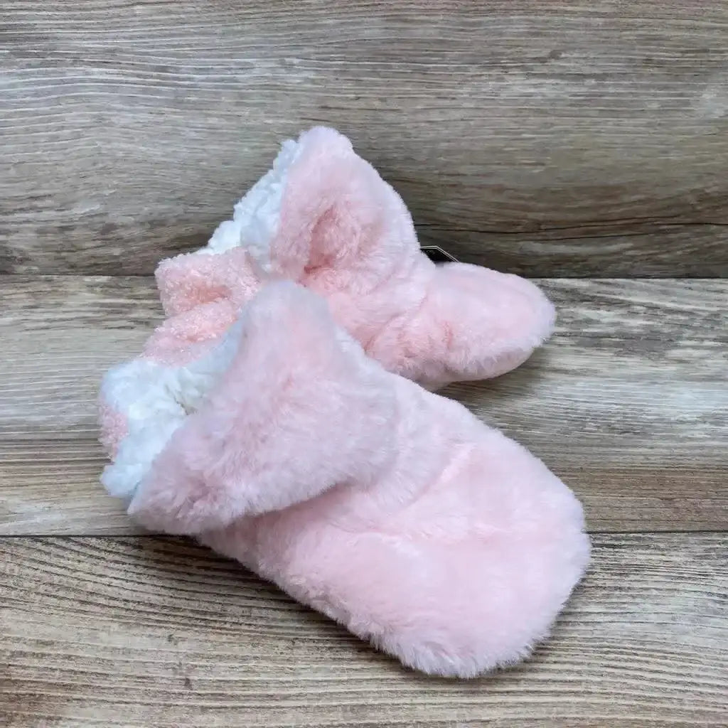 Three-quarter view of pink infant plush slippers showcasing white sherpa lining and gripper soles on light wood background