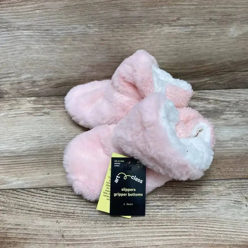 Top-front view of pink baby slippers showing gripper bottoms and white sherpa lining on wood floor background