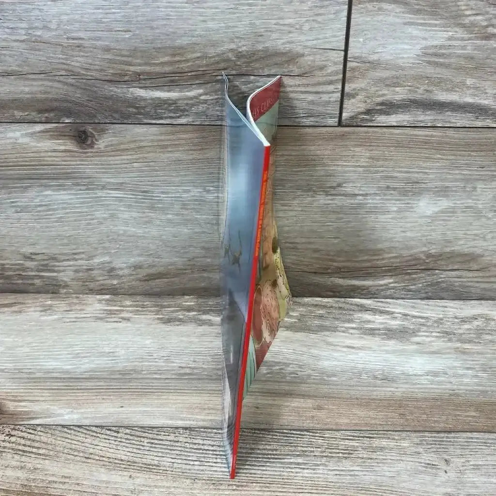 Side view of Yes, Virginia, There Is a Santa Claus paperback book showing its red cover edge and pages on wood grain