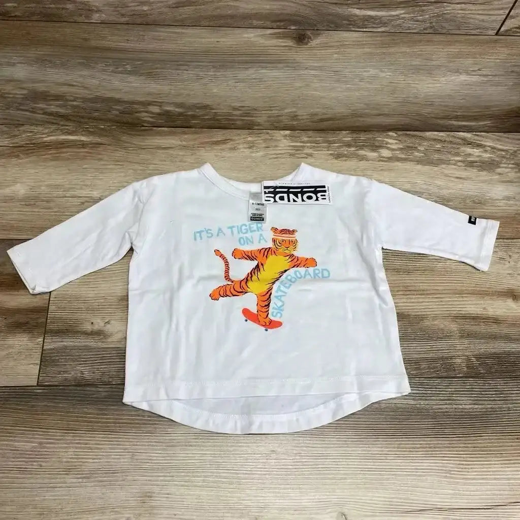 Front view of white Bonds baby long sleeve shirt showcasing orange tiger on a skateboard graphic with tag on wood floor