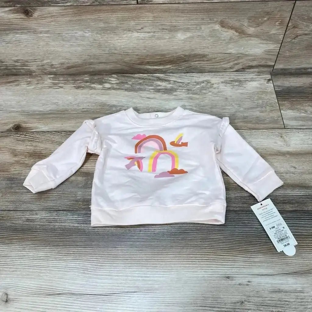 Front flat-lay of pink Cat & Jack baby sweatshirt (3-6M) showcasing rainbow and cloud graphic and ruffled shoulder detail on wood floor background
