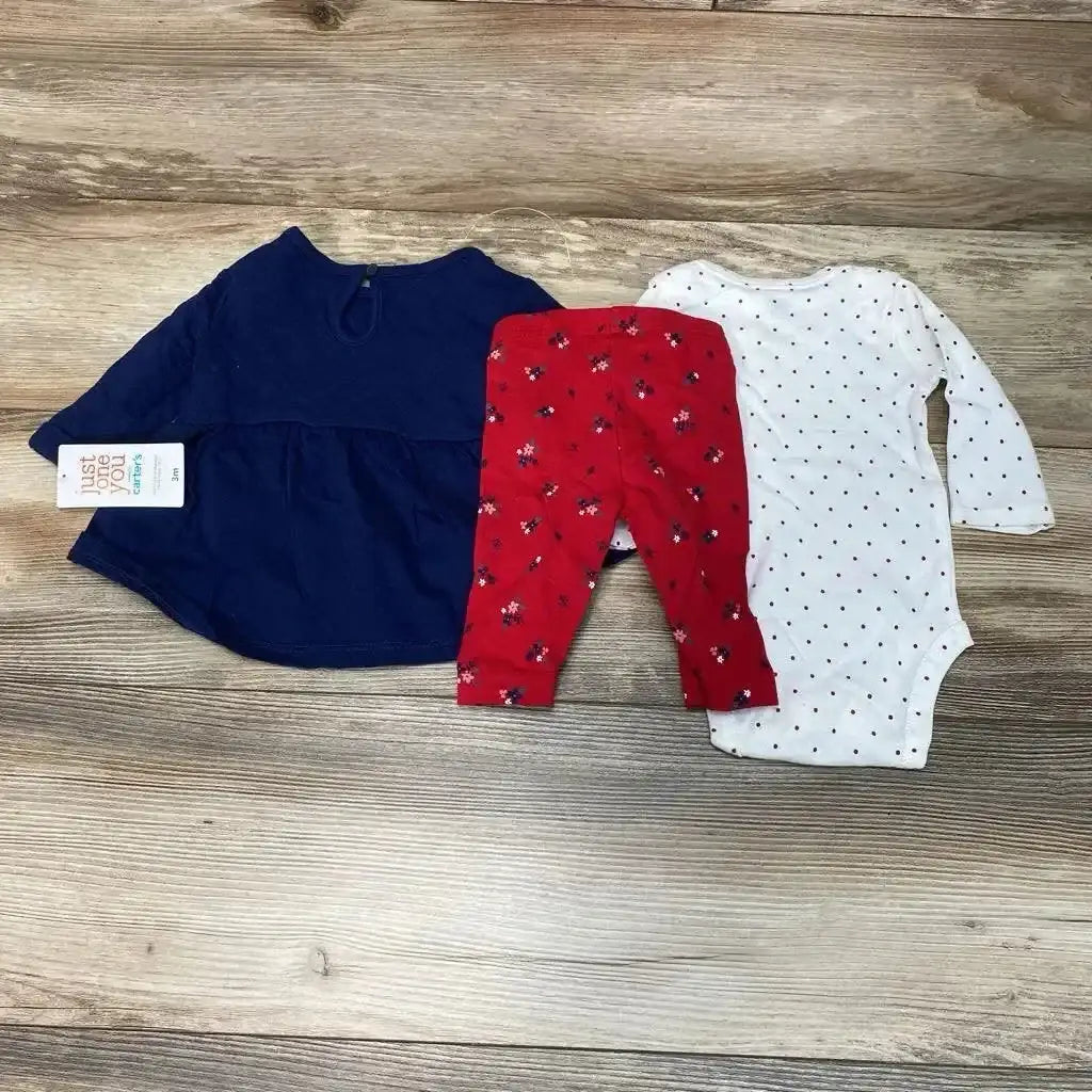 Flat lay of 3-piece baby outfit: navy long-sleeve tunic, white polka-dot bodysuit, red floral pants on wood background
