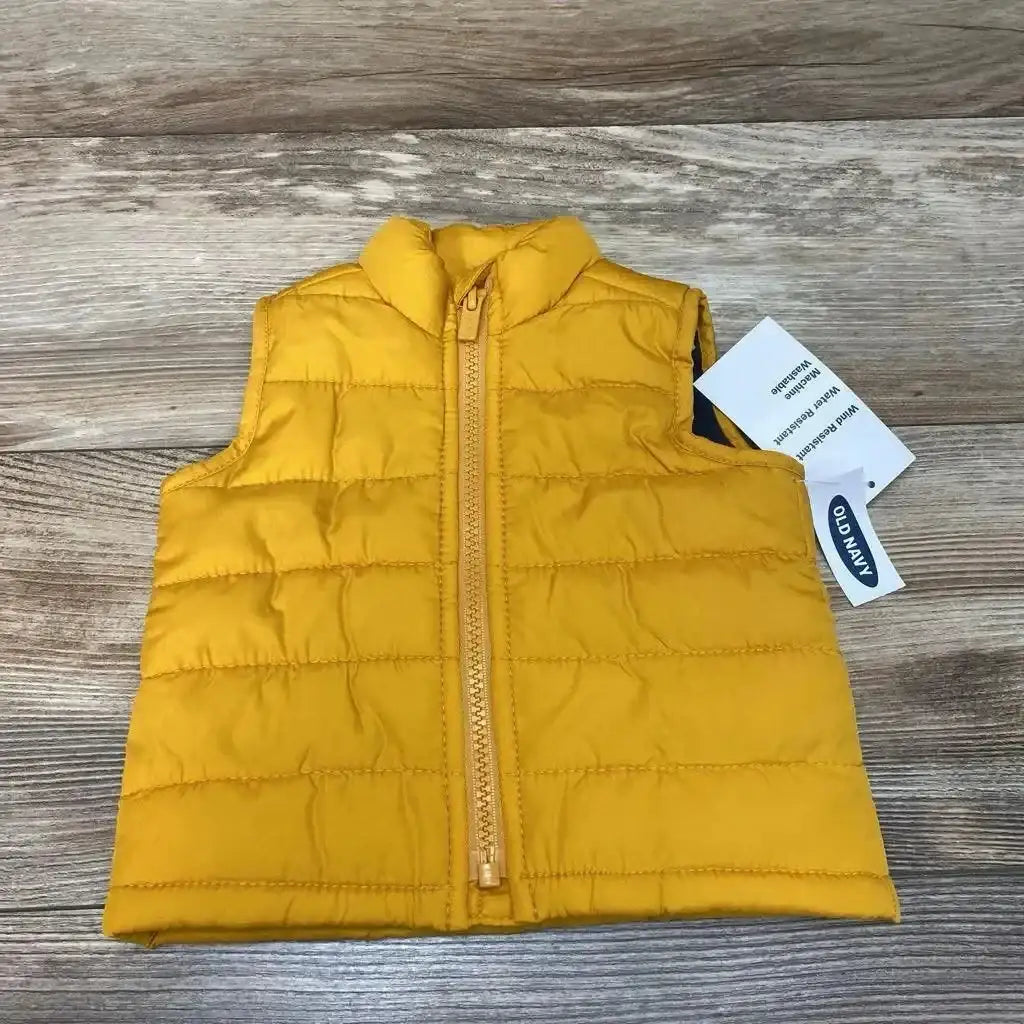 Front view of yellow Old Navy baby puffer vest showcasing center zipper and quilted horizontal baffles on wood background