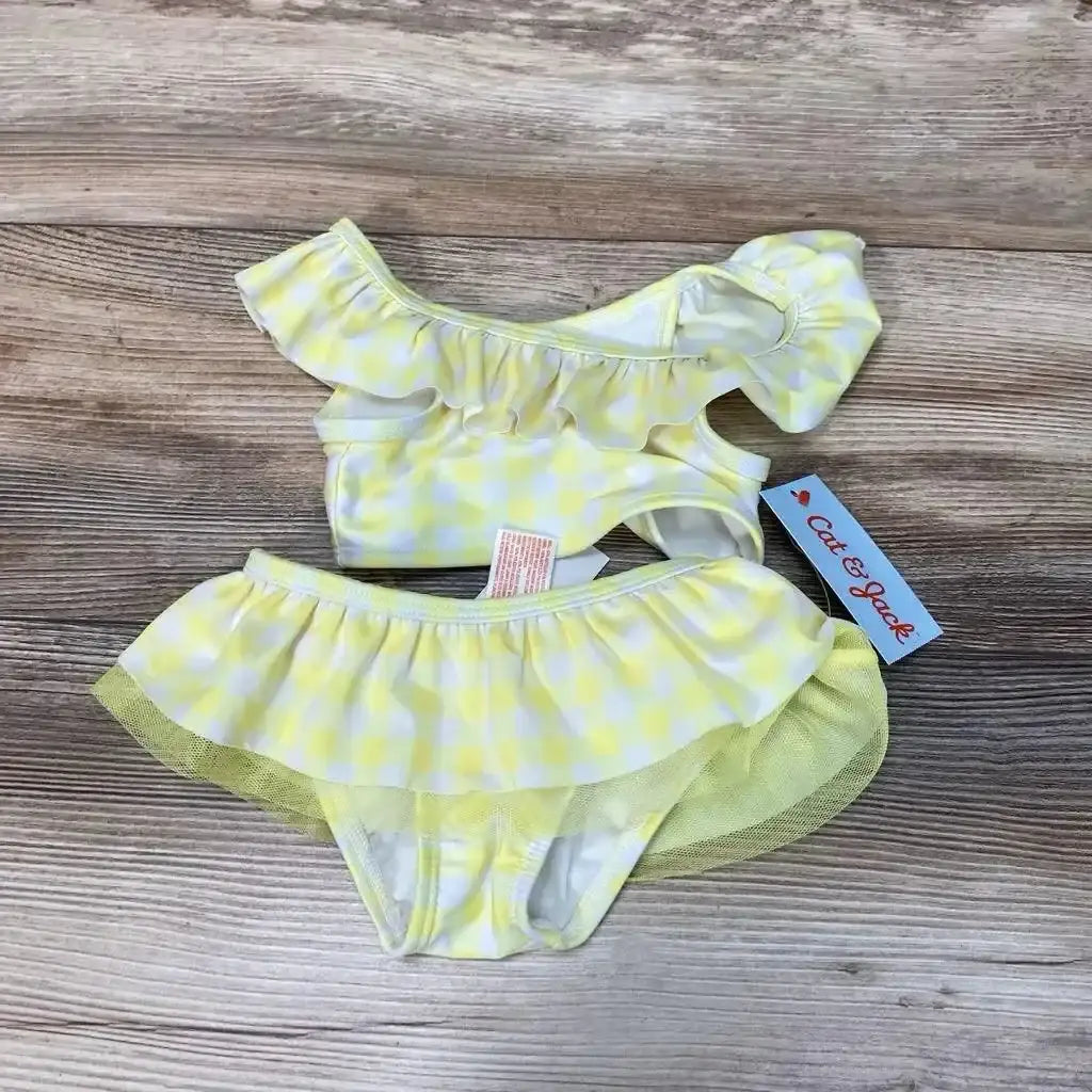 Flat lay of yellow gingham 2-piece baby bikini (size 12M) showing ruffle one-shoulder top and skirted mesh bottoms on wood background