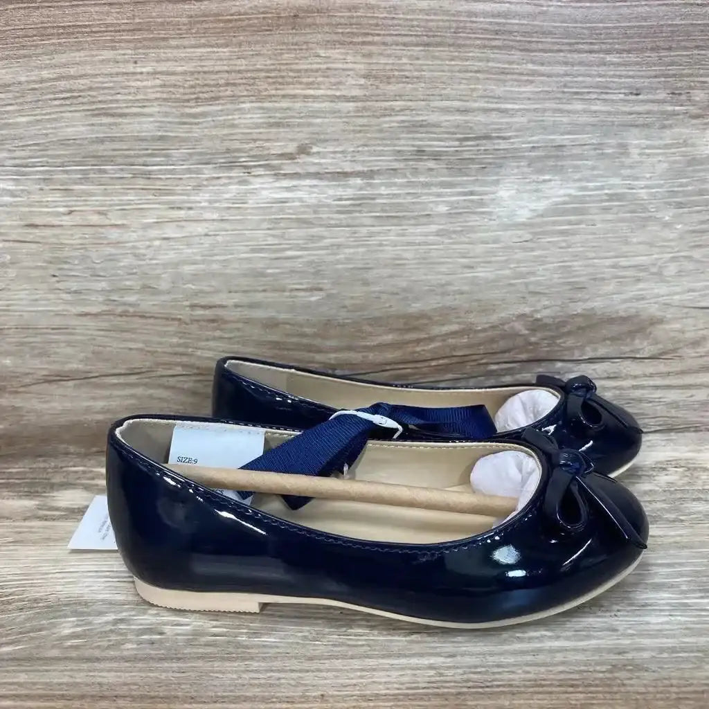 Side view of pair of navy patent bow ballet flats size 9C showing patent finish and toe bows on wood-grain surface