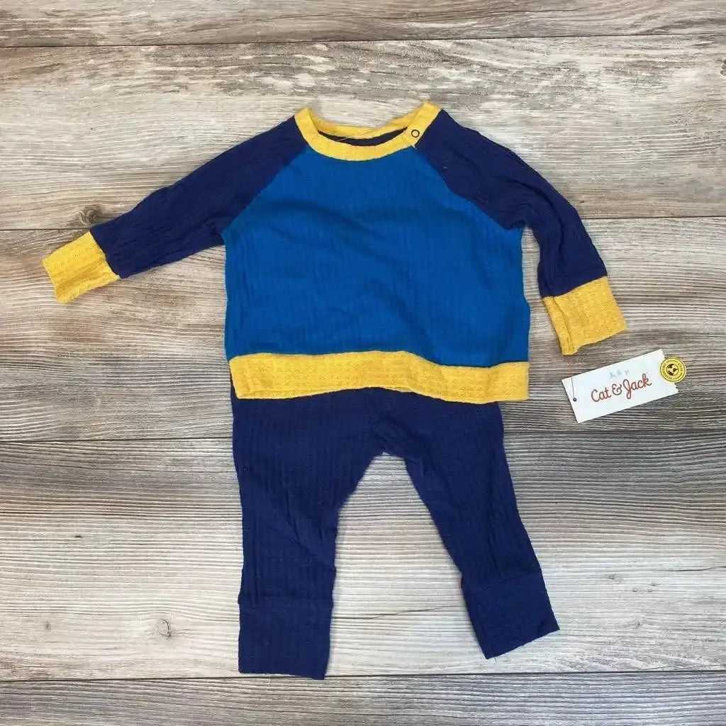 Flat lay of blue and navy waffle-knit baby shirt and pants set with yellow trim and shoulder snap on wood background