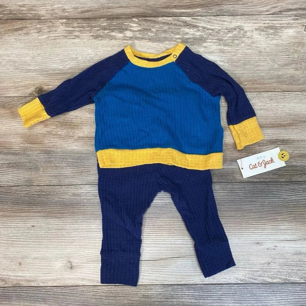 Flat lay of blue and navy waffle-knit baby shirt and pants set with yellow trim and shoulder snap on wood background