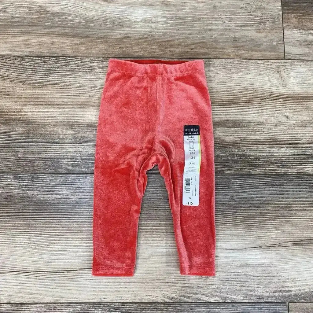 Front view of NWT Okie Dokie velour leggings in coral pink showcasing elastic waistband and brand hangtag on wood plank floor