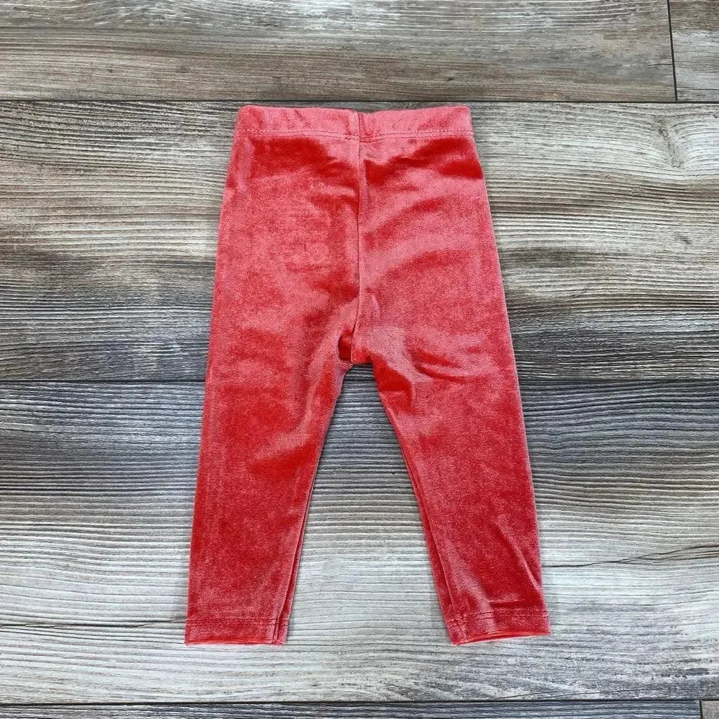 Flat lay of red velour baby leggings (3M) showing soft plush fabric, elastic waistband, and tapered legs on wooden background