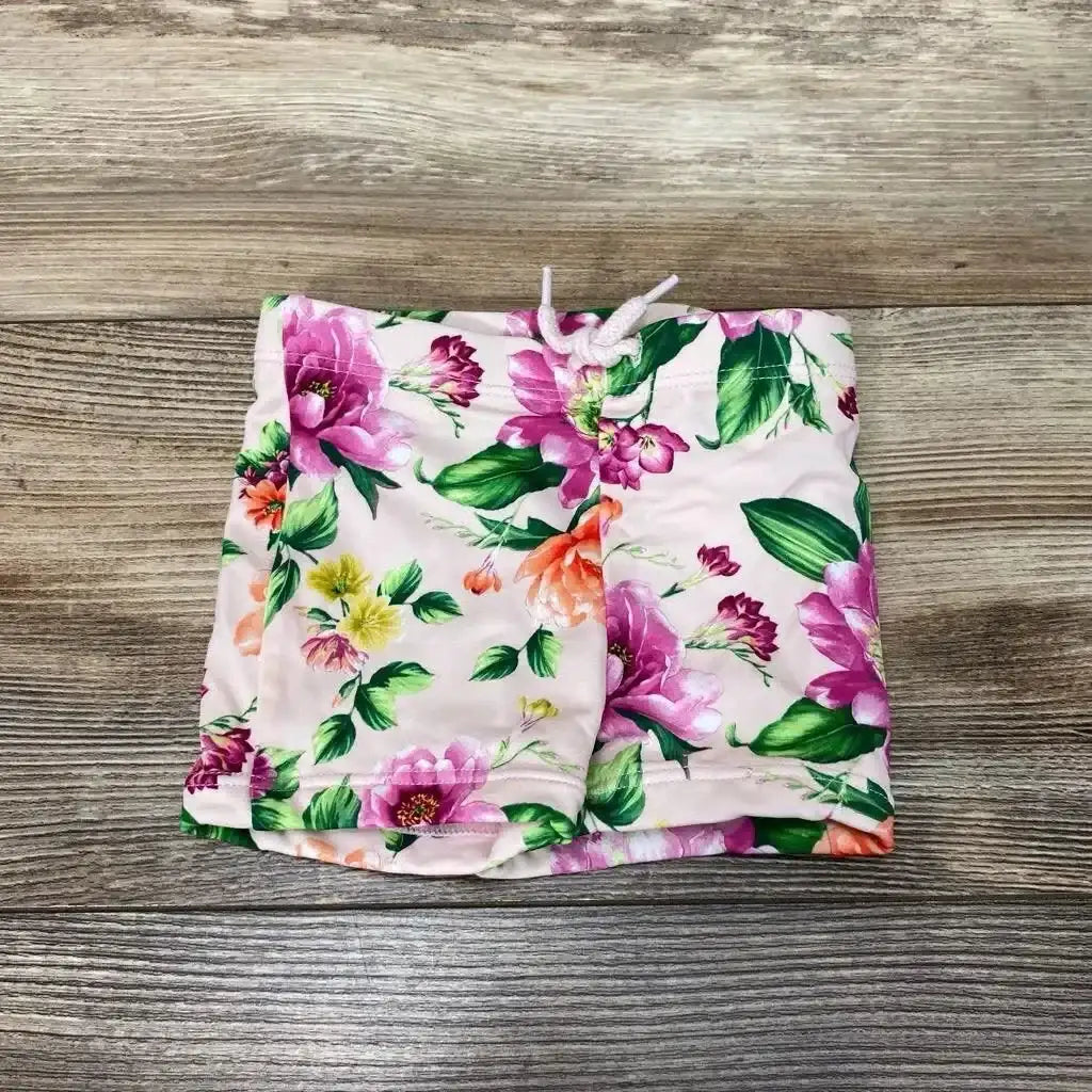 Flat lay of Janie and Jack floral swim shorts in pink with tropical floral print and drawstring on wood plank floor sz 6-12m