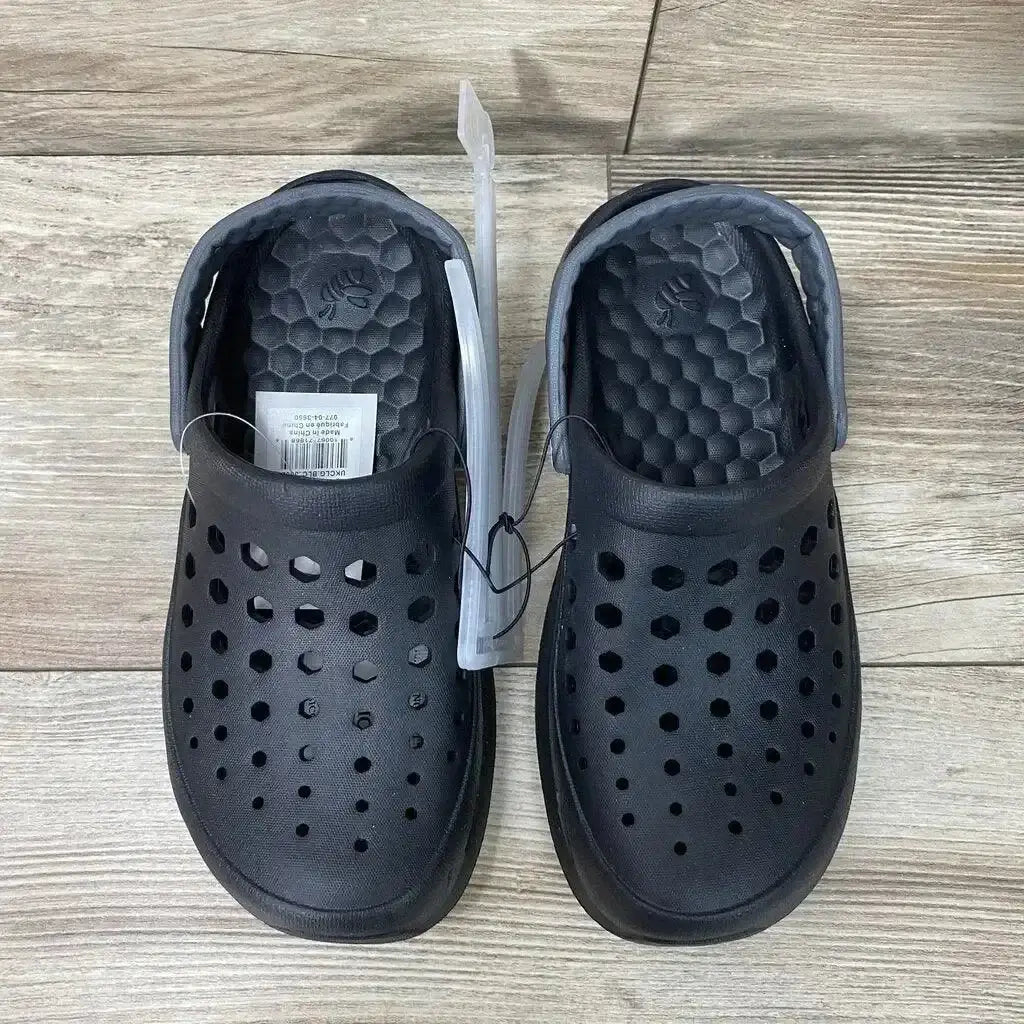 Top view of NEW Joybees Unisex Varsity Clogs showcasing black perforated clogs with heel straps and hangtag on wood plank floor