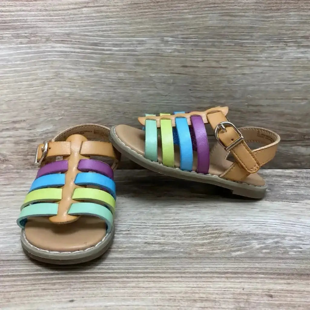 Top view of Cat & Jack Sandals size 5c with rainbow strappy upper tan footbed and buckle closure on wood plank floor