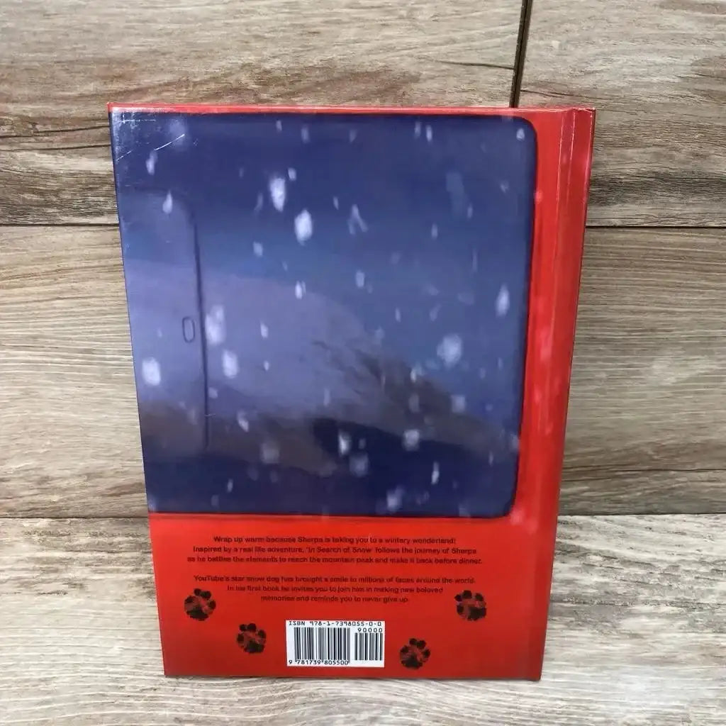 Back view of Sherpa, In Search of Snow hardcover children's book showing red spine, paw-print design and barcode on wood background