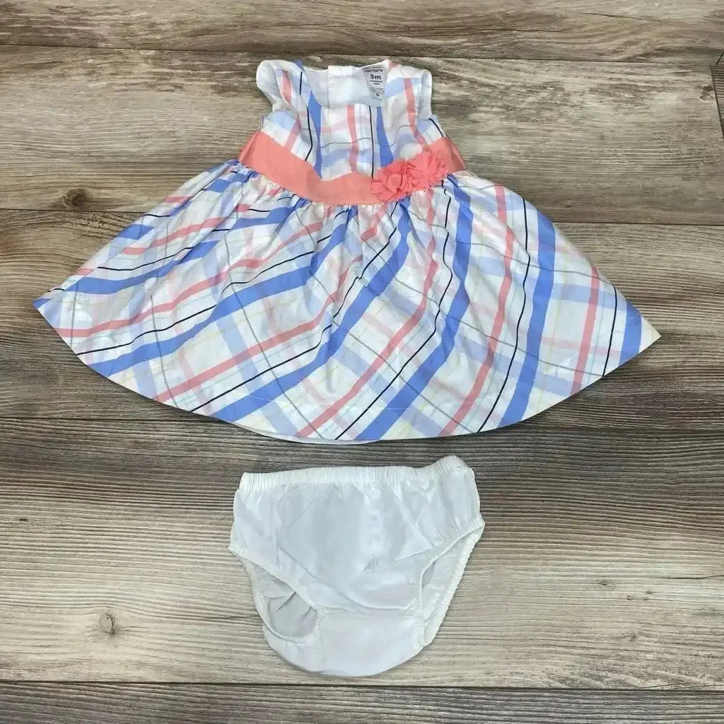 Front view of Carter’s two-piece plaid dress and bloomers showcasing a coral waistband and flower accent on a wood surface