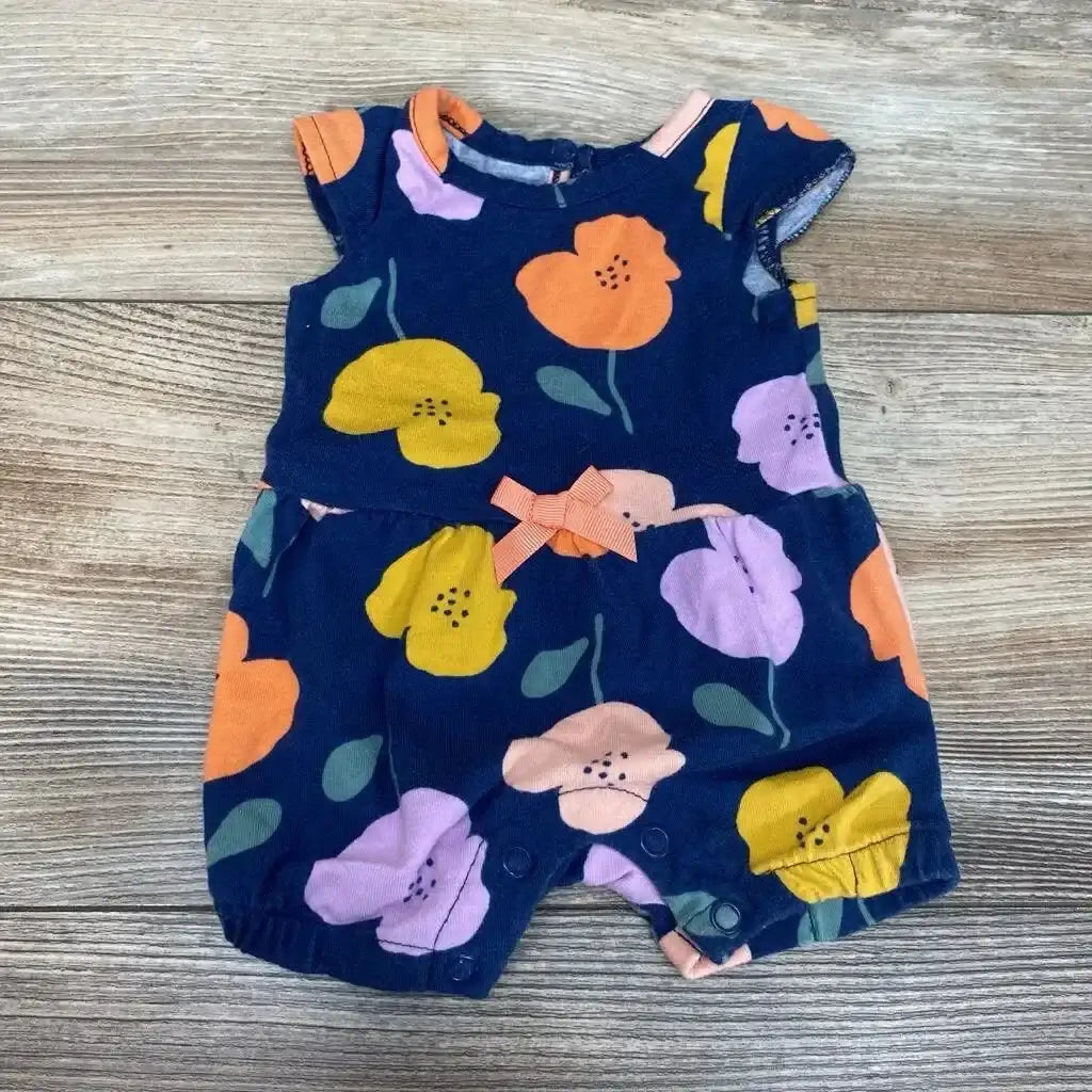 Top-down view of newborn navy floral romper with orange and yellow flowers, front bow and snap crotch on wood background