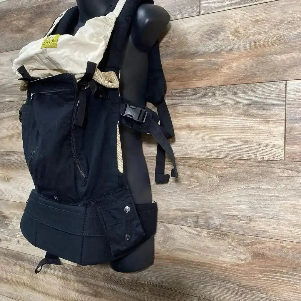 Side view of LILLEbaby 6-Position Complete Airflow carrier showing beige hood, padded waist belt and straps on wood floor