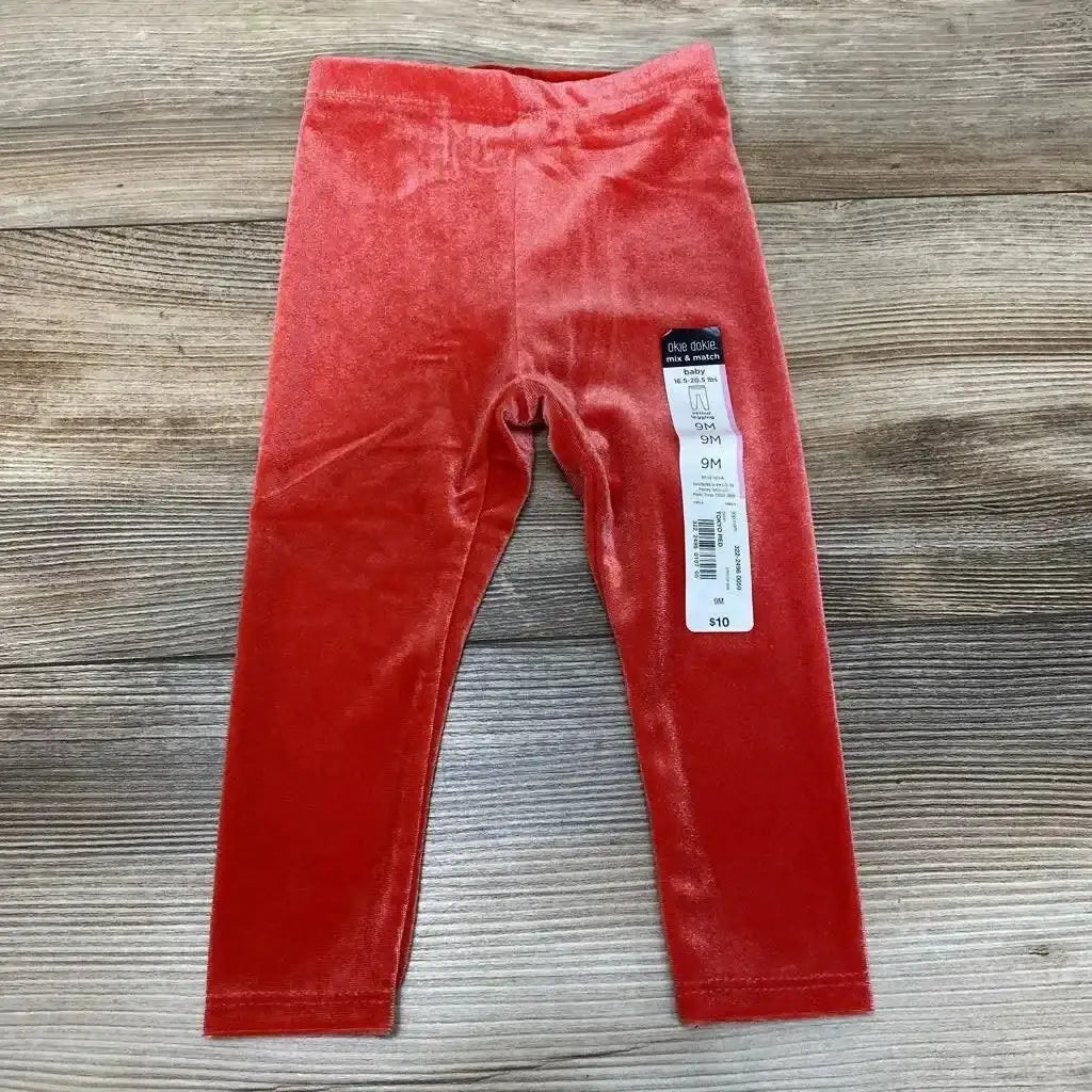 Flat lay of red velour baby leggings size 9M showing elastic waist and plush fabric on wood background
